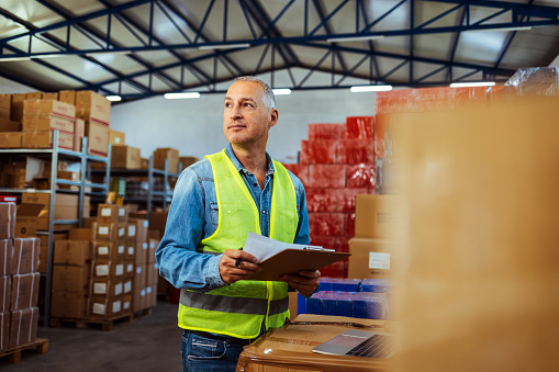 Happy mature worker with a checklist in distribution warehouse