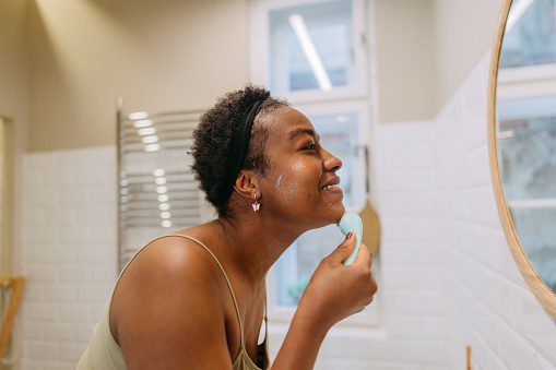 Photo of a young woman washing her face in a bathroom.