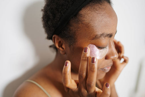 Photo of a young woman applying under-eye patches as a part of her beauty routine.