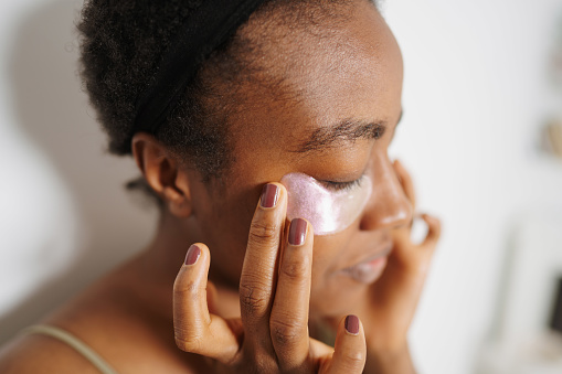 Photo of a young woman applying under-eye patches as a part of her beauty routine.