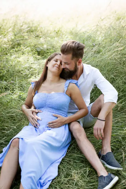 Photo of young couple in love sitting in high flower meadow in summer cuddling and woman is pregnant