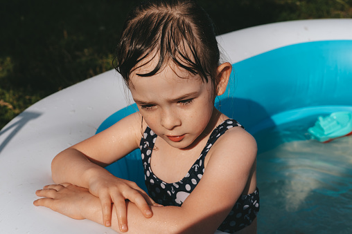 Portrait of a child in the pool on a summer sunny day. Girl looking to the side