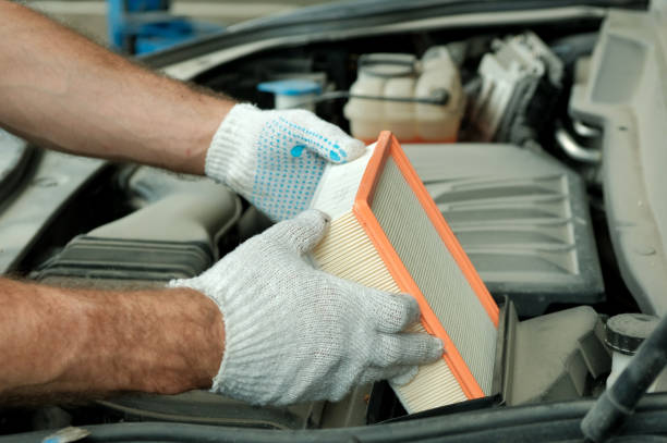 An auto mechanic installs a new air filter during car maintenance at a service station.