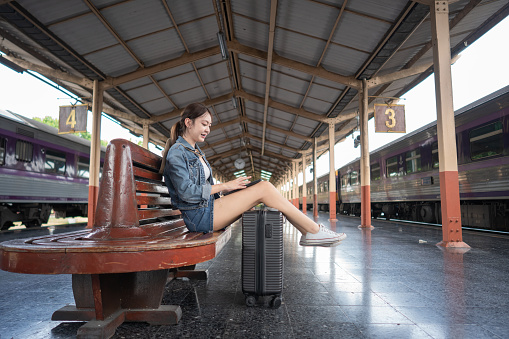 Asian young woman traveler sitting in a train station and using a digital tablet. Travel concept.
