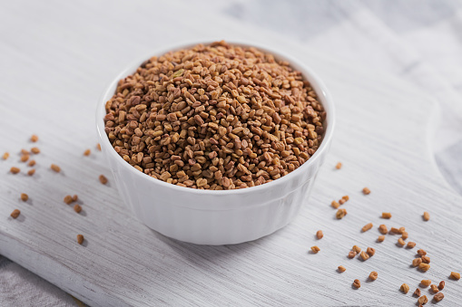 Bowl of fenugreek dry seeds on white wooden background. Healthy food, Ayurveda and alternative medicine concept