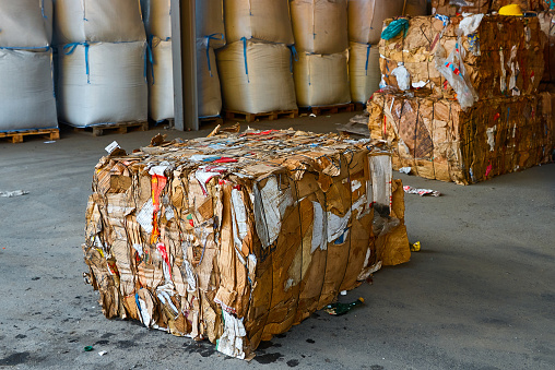 Block of pressed waste paper and cardboard boxes on floor in processing plant warehouse closeup. Recycling resources in storage. Sustainable industry