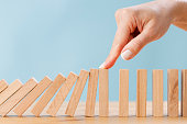 Business woman's finger try to stopping falling wooden dominoes blocks for business solution concept