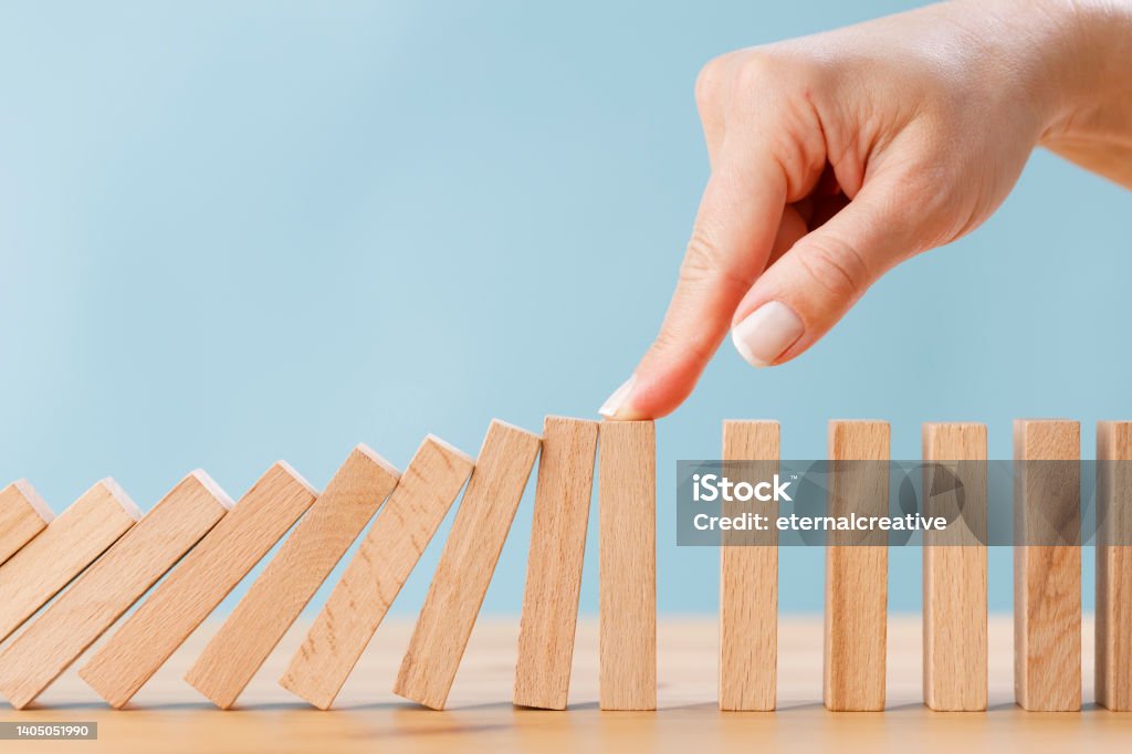 Business woman's finger try to stopping falling wooden dominoes blocks for business solution concept Business woman's finger try to stopping falling wooden dominoes blocks for business solution concept. Business crisis effect or risk protection concept Domino Stock Photo