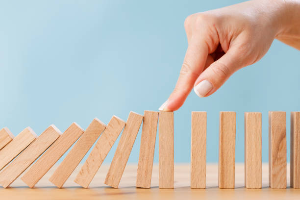 business woman's finger try to stopping falling wooden dominoes blocks for business solution concept - dominó imagens e fotografias de stock