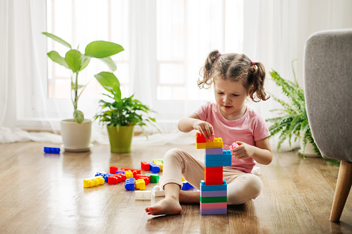 A little girl is sitting on the floor in the playroom and playing with colorful cubes, a constructor. Educational games, education.