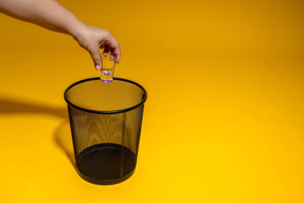istock The hand throws a glass stack into the trash. The tequila glass is thrown into the office wastebasket. The concept of getting rid of glass and fighting alcoholism. 1405060112