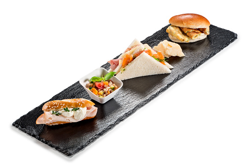 Black stone rectangular tray with snack Pretzel turkey flaky cheese sandwiches salmon pearl spelled vegetables milk sandwiches omelette on white background