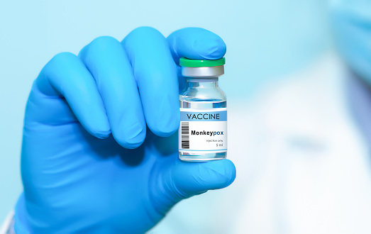 La mano del médico en un guante médico sostiene una botella con la vacuna Monkeypox y la viruela sobre un fondo azul. photo