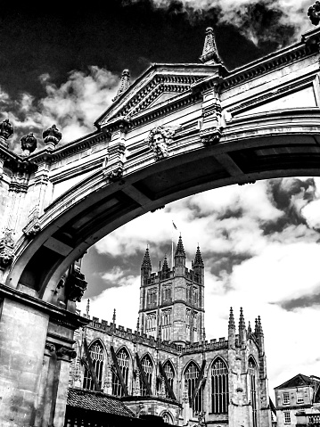 The abbey of Bath, England, UK, as seen through an ornate architectural arch, in black and white. The Church is part of the former Benedictine Abbey, which date out of the middle ages. During this time the city was a well-known for its wool industry, before it become a spa city once again in the Gregorian and Victorian ages.