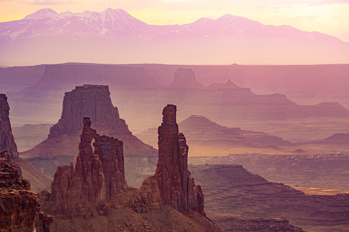 Aerial view at Canyonlands National Park at sunrise. In the front standing rocks and desert landscape, in the back snowcapped mountains.