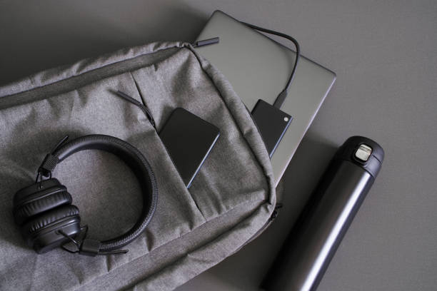 istock Small textile urban backpack with a steel-colored laptop, an external SSD drive, smartphone, wireless headphones and thermos. Traveling with gadgets. Hand luggage at the airport. Copy space 1405067511