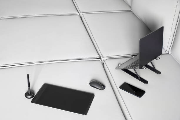 Thin laptop on a stand and graphics tablet with stylus on a light modular sofa. Top view. Concept of a comfortable remote work of a designer and access to the Internet from home. Copy space