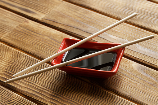 Red Japanese sauce bowl - seyuzaru, chopsticks - varibashi and soy sauce on a wooden table made of pine boards. Selective focus. Close-up