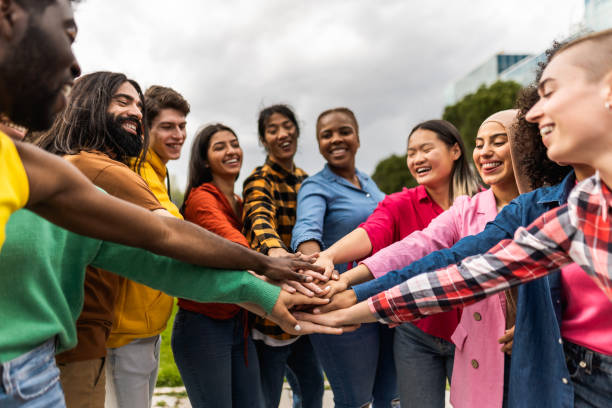 Young multiracial community of friends having fun stacking hands together outdoor - Friendship and diversity concept stock photo