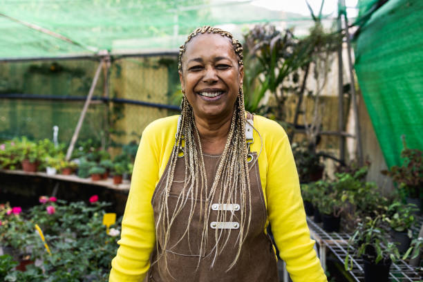 花畑の店で働きながらカメラの前で微笑む幸せなアフリカ人女性 - gardening single flower house flower ストックフォトと画像
