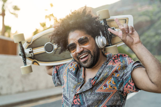 Happy Afro skater having fun listening to music with headphones during summer time - Youth people lifestyle concept stock photo