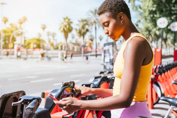 trendy african american woman using her phone to unblock bike from a bike rack