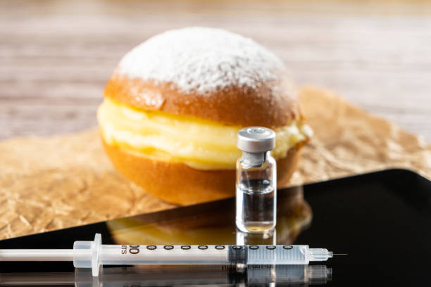 nahaufnahme einer spritze und ampulle mit insulin auf der tablette. im hintergrund ein brasilianischer sahne-donuts. - syringe vaccination vial insulin stock-fotos und bilder