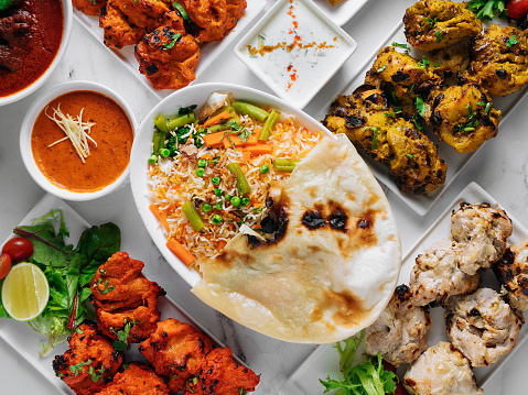 Assorted famous indian and pakistani food table vegetable biryani, Butter Chicken, paneer Chicken Tikka boti kebab, lime, Kali Mirchi, tomato sauce, raita, roti, salad, top view on grey background