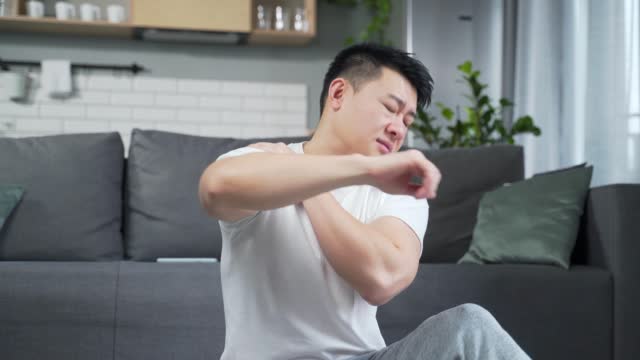 Young asian man exercise Stretch the back pain at home indoors. Athletic fitness male suffering feel hurt sudden ache shoulder and joints Muscle strain