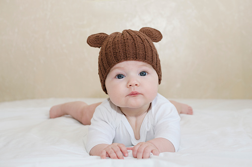 Portrait of a cute newborn baby in a brown knitted hat with ears lying on his stomach on a bed with ears close-up, teddy bear.