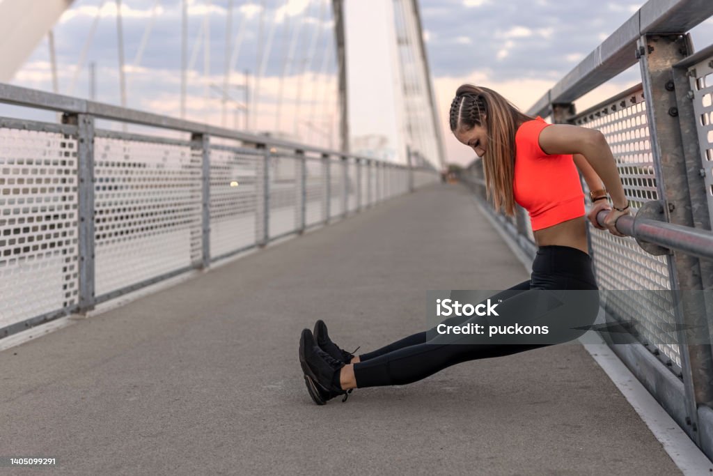 Young Happy Focused Fitness Girl In Black Yoga Pants And Orange Short Shirt  Work Out And Stretch Her Body On The Bridge Footpath During The Day Front  View Stock Photo - Download