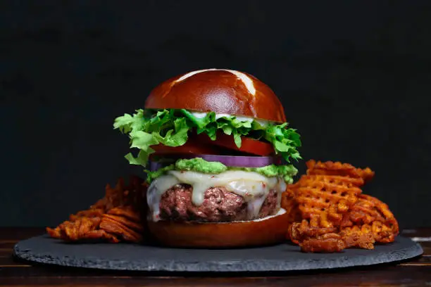Photo of Gourmet Burger with Preztel Roll surrounded by sweet potato waffle fries