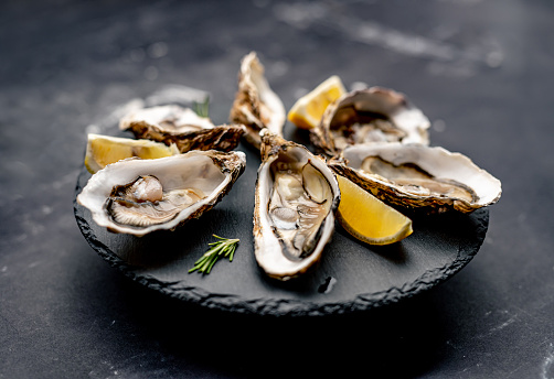 Oysters with lemon served on black round platter. Luxury delicatessen seafood