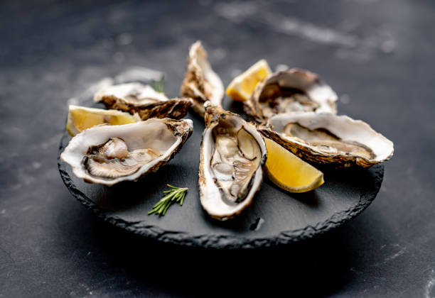 Oysters with lemon on platter Oysters with lemon served on black round platter. Luxury delicatessen seafood oyster stock pictures, royalty-free photos & images