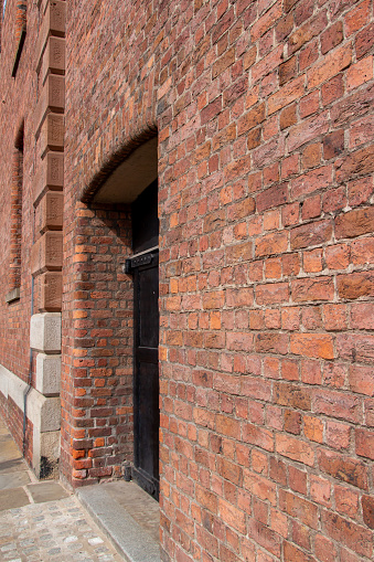 This image shows an old exterior European stone brick wall texture background in an English bond brickwork pattern, with weathered bricks and view of an entrance doorway.