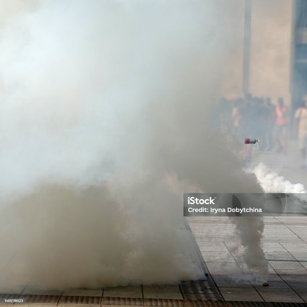 Tear gas bomb attacks on protesters. Tear gas bombs flying in air and smoking on the asphalt on background of people Gas Stock Photo