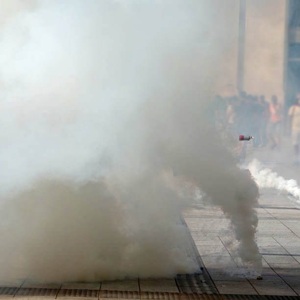 Tear gas bomb attacks on protesters. Tear gas bombs flying in air and smoking on the asphalt on background of people tear gas stock pictures, royalty-free photos & images