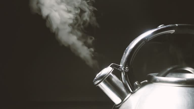 Boiling steel silver kettle with a whistle with steam close-up on a black background. 4k raw slow motion video with speed ramp effect. Filmed on high speed cinema camera.