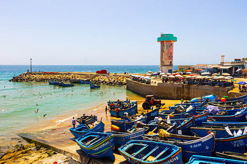 Agadir, Morocco - 14 AUGUST 2020 : The harbor of Imesouane. Blue boats, seagulls, a tractor, coffee, fishermen, people swimming and a control tower