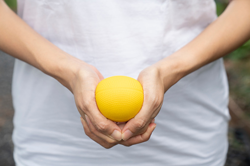Hands of a woman squeezing a yellow stress ball, close up
