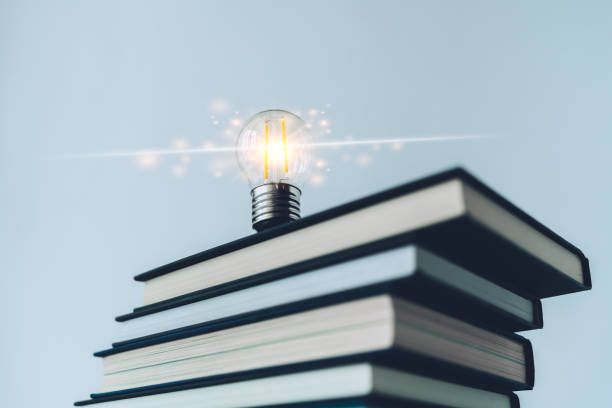 istock Glowing lightbulb or bright lamp with book or textbook. Skill improvement for student or businessperson. Studying and training course online at home. Business success idea, education learning concept 1405145371