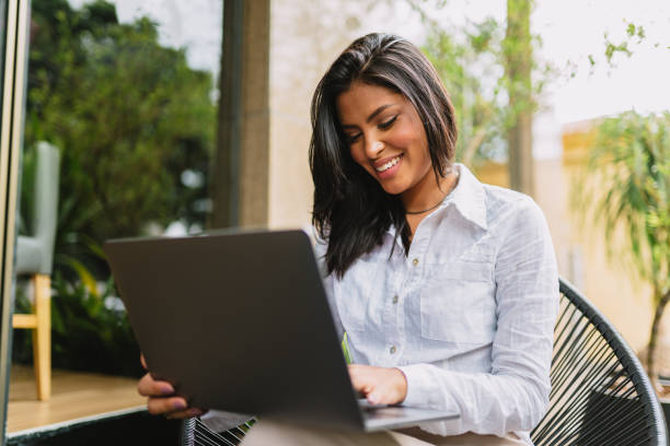 istock Nomad on work. Confident young Latin woman making video call on laptop while sitting by window in cafe. 1405154715