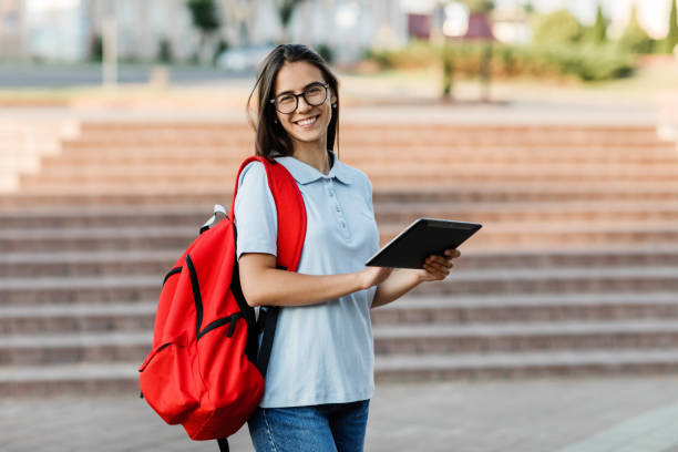 한 학생 소녀가 도시를 산책하는 동안 태블릿에 메시지를 씁니다. - student printed media walking clothing 뉴스 사진 이미지