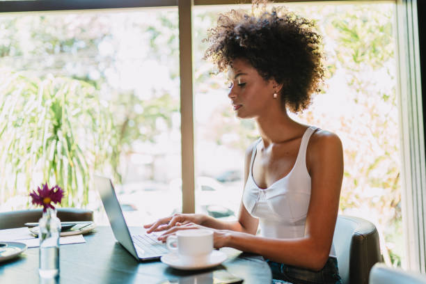 istock Nomad on work. Confident young Latin woman making video call on laptop while sitting by window in cafe. 1405155549