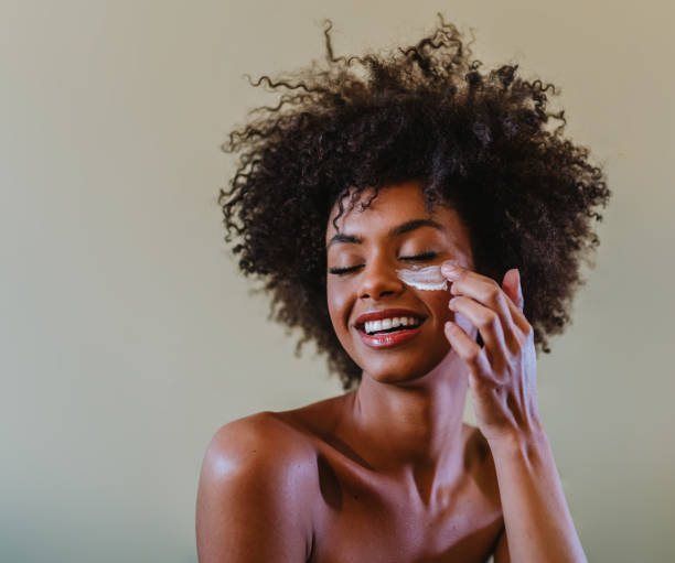 close up portrait of latina woman applying facial cream to her face. - beauty treatment moisturizer human skin cosmetics imagens e fotografias de stock