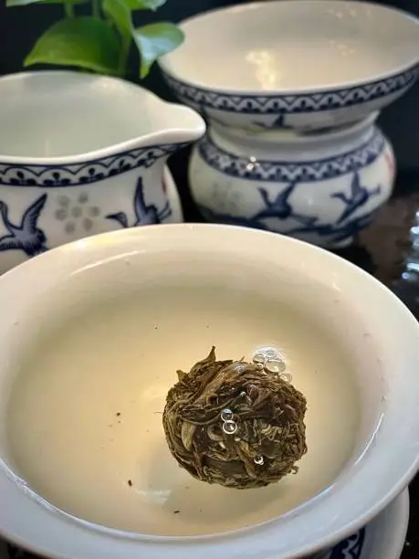 June 3, 2022; Bejing China; An image of a raw Pu er dragonball expanding in hot water in a gaiwan teapot, emitting bubbles from the expanding leaves.