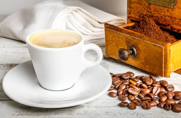 A cup of hot coffee and an old coffee grinder on a white wooden table