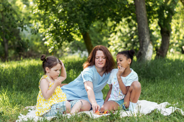Multiracial mother and daughters is having a picnic on a summer day and eating fruit.Family, summer,diverse people concept