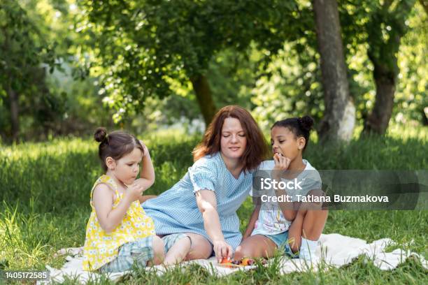 Multiracial mother and daughters is having a picnic on a summer day and eating fruit.Family, summer,diverse people concept