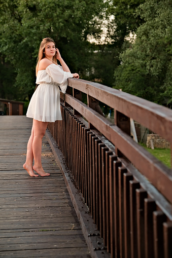 a beautiful girl in a white dress stands on a wooden bridge.